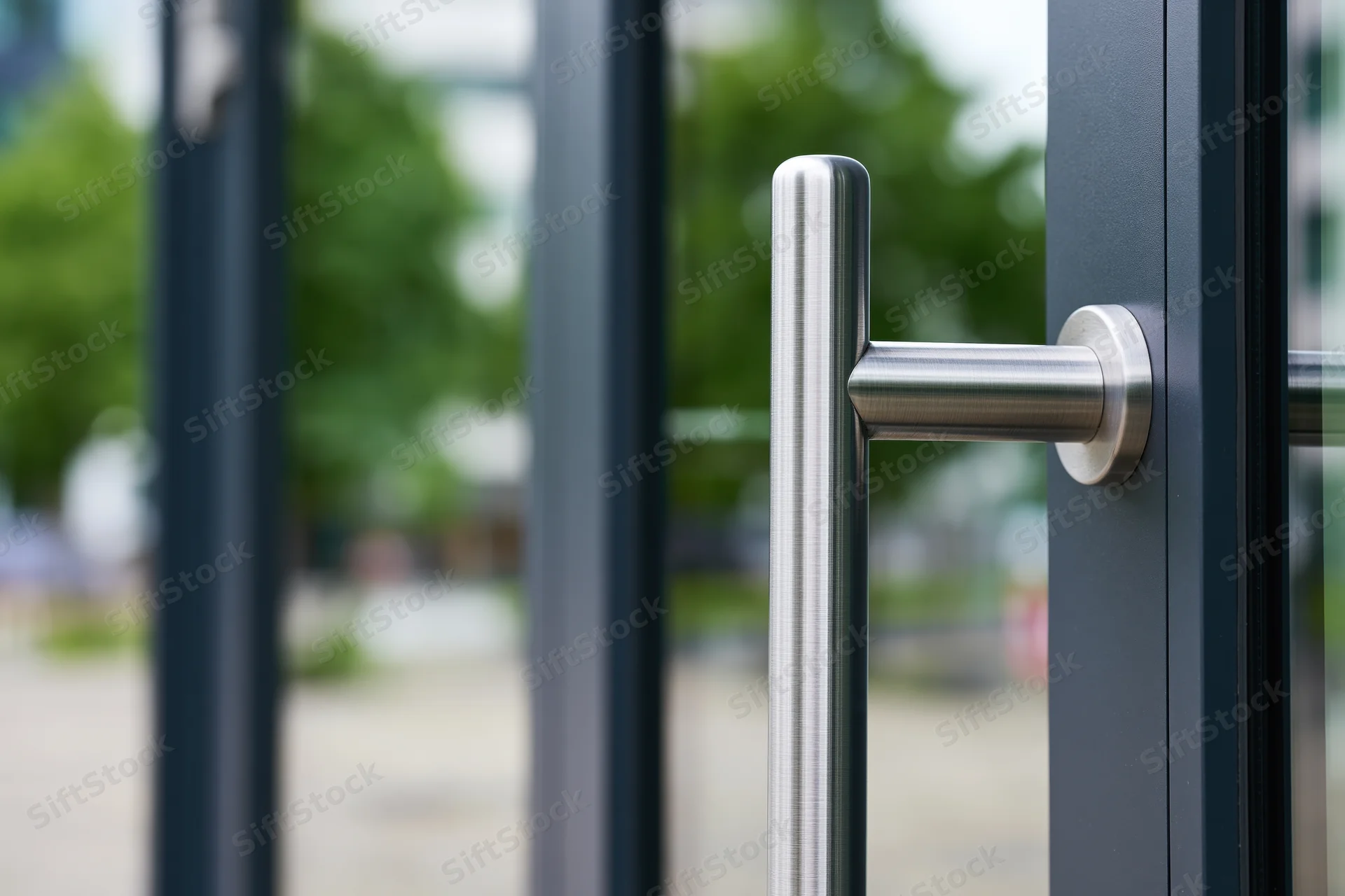 Close-up of a brushed stainless steel vertical door pull handle on a modern glass door frame