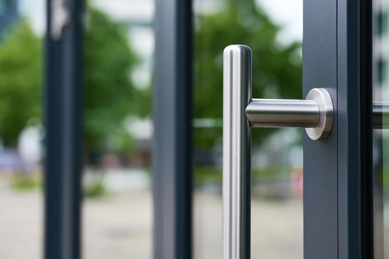 Close-up of a brushed stainless steel vertical door pull handle on a modern glass door frame