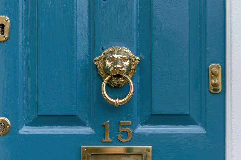 Close-up of a blue front door with a brass lion knocker and number 15 plate