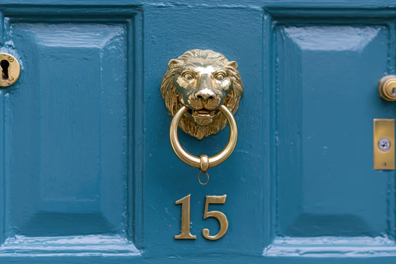 Close-up of a teal front door with a brass lion knocker and number 15