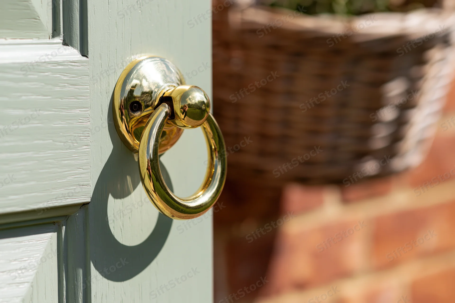 Polished brass door knocker on sage green wooden door with wicker basket in background