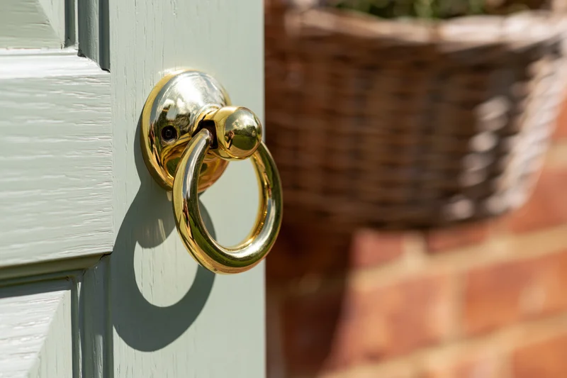 Polished brass door knocker on sage green wooden door with wicker basket in background