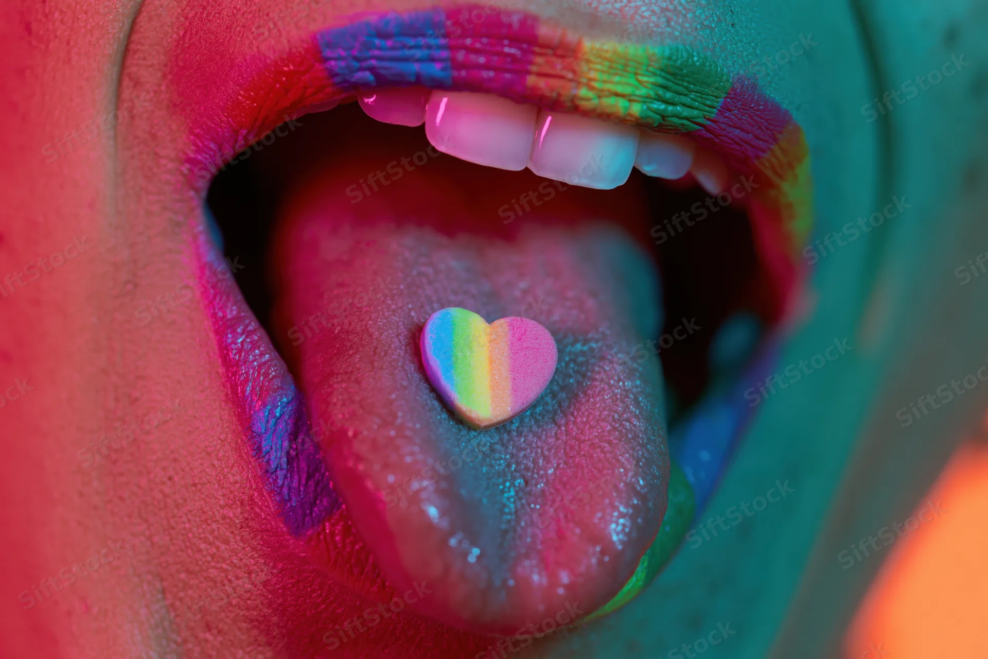 Woman with open mouth showing tongue holding rainbow heart candy