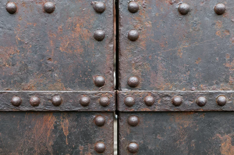 Close-up of two weathered steel gate panels meeting at a seam with rivets and rusted surface