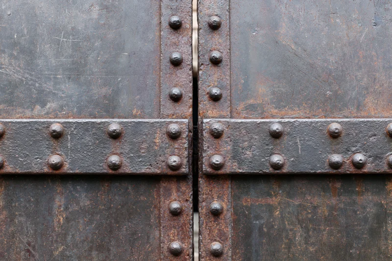 Close-up of two weathered steel gate panels meeting at a narrow gap with rivets and horizontal bars