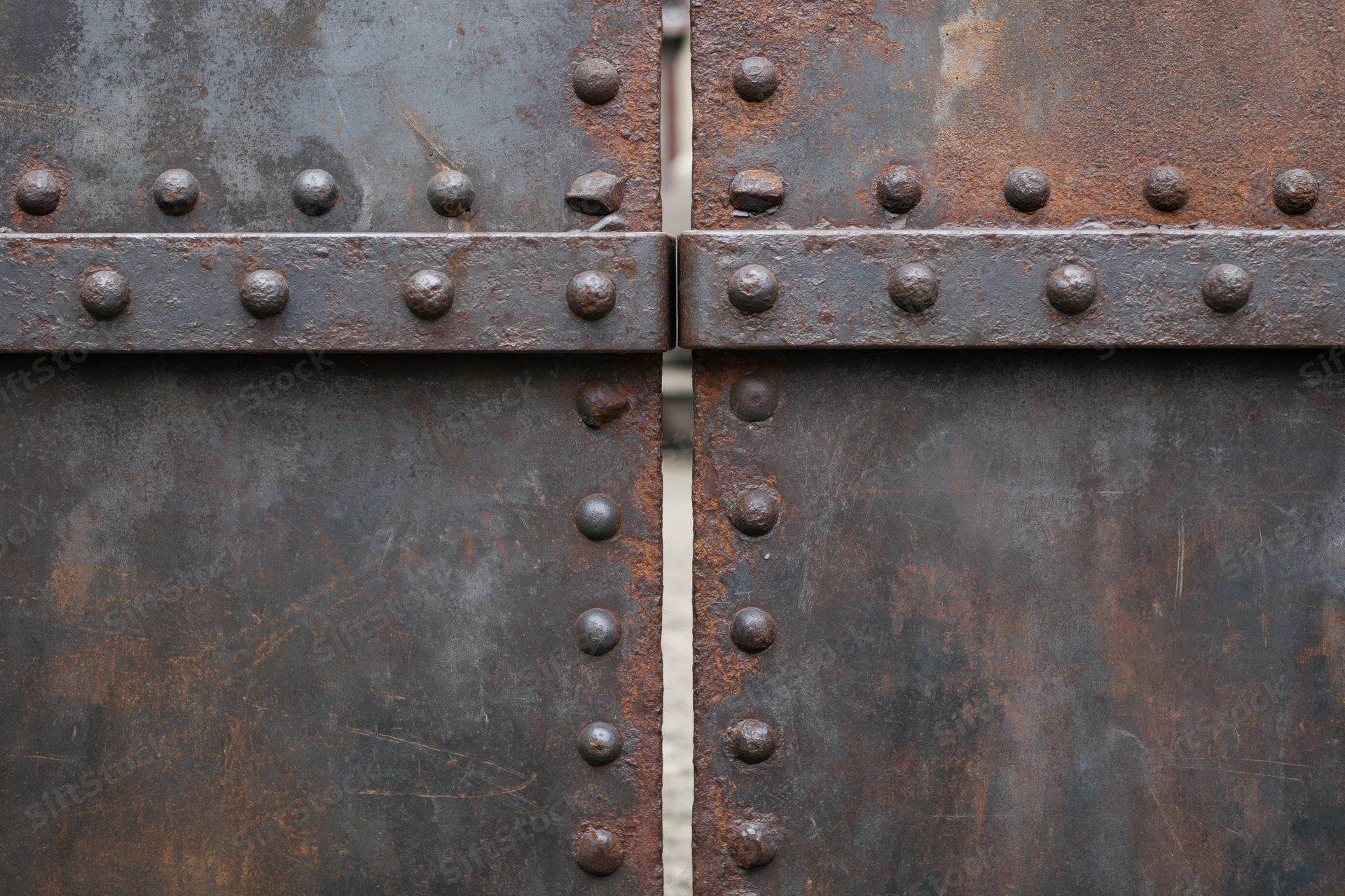 Close-up of two weathered steel gate panels meeting at a seam with rivets and rust