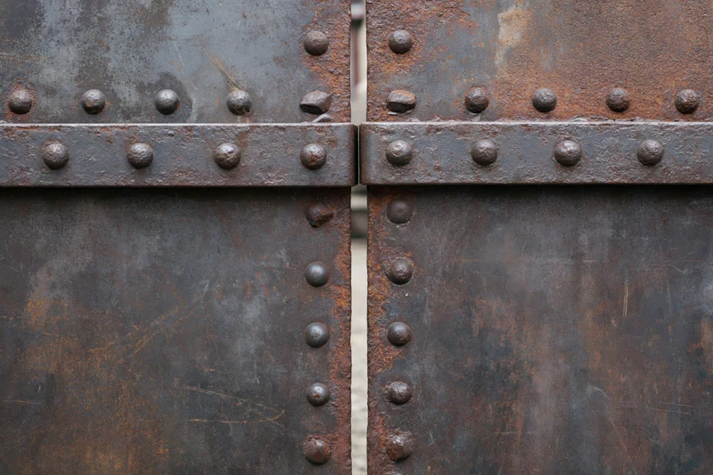 Close-up of two weathered steel gate panels meeting at a seam with rivets and rust