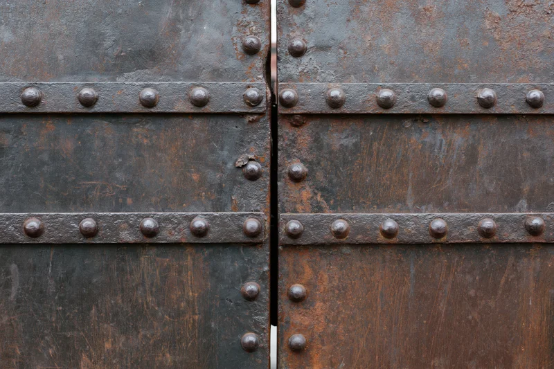 Weathered steel gate panels with rivets meeting at a narrow gap