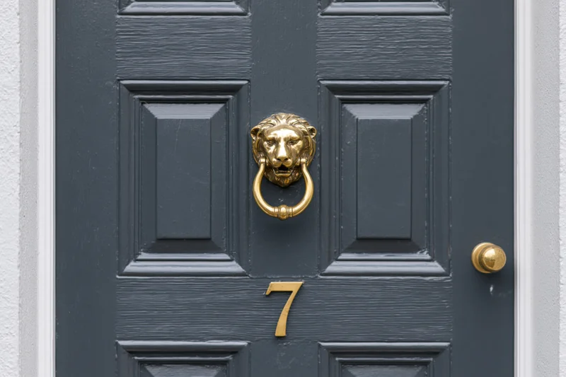 Dark charcoal grey wooden front door with brass lion knocker and number seven, framed by white trim