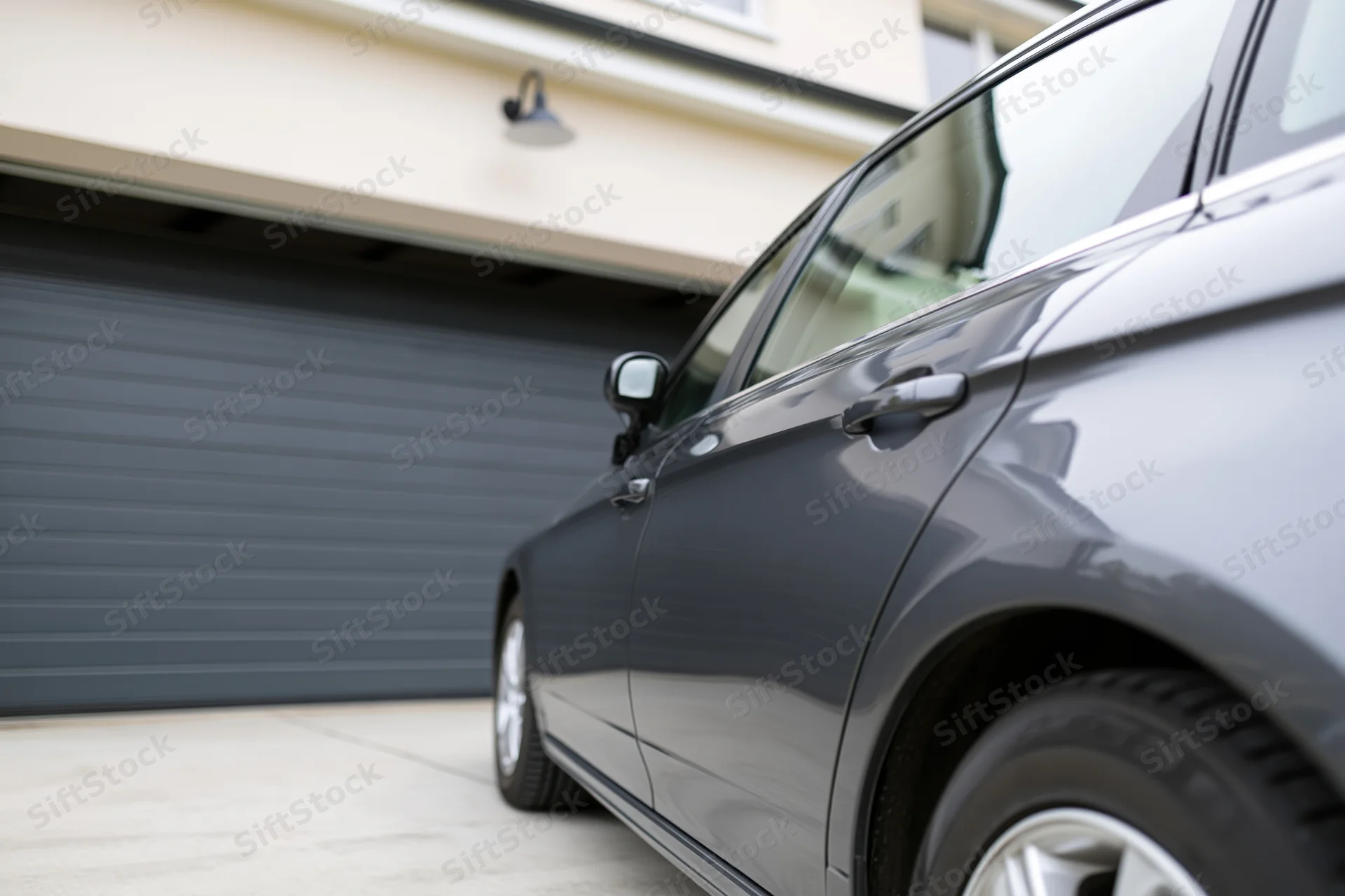 Dark grey sedan parked in front of a residential garage with driveway and house exterior visible