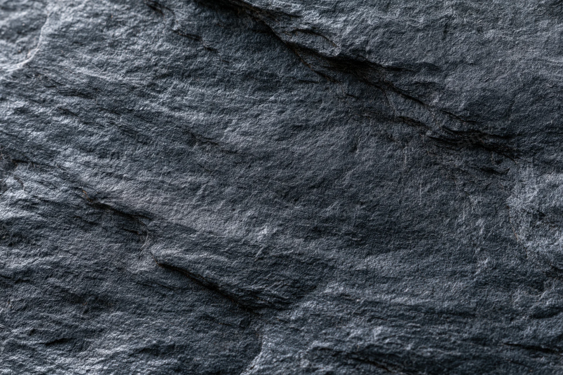 Dark slate rock surface with natural texture and layered fractures filling the frame