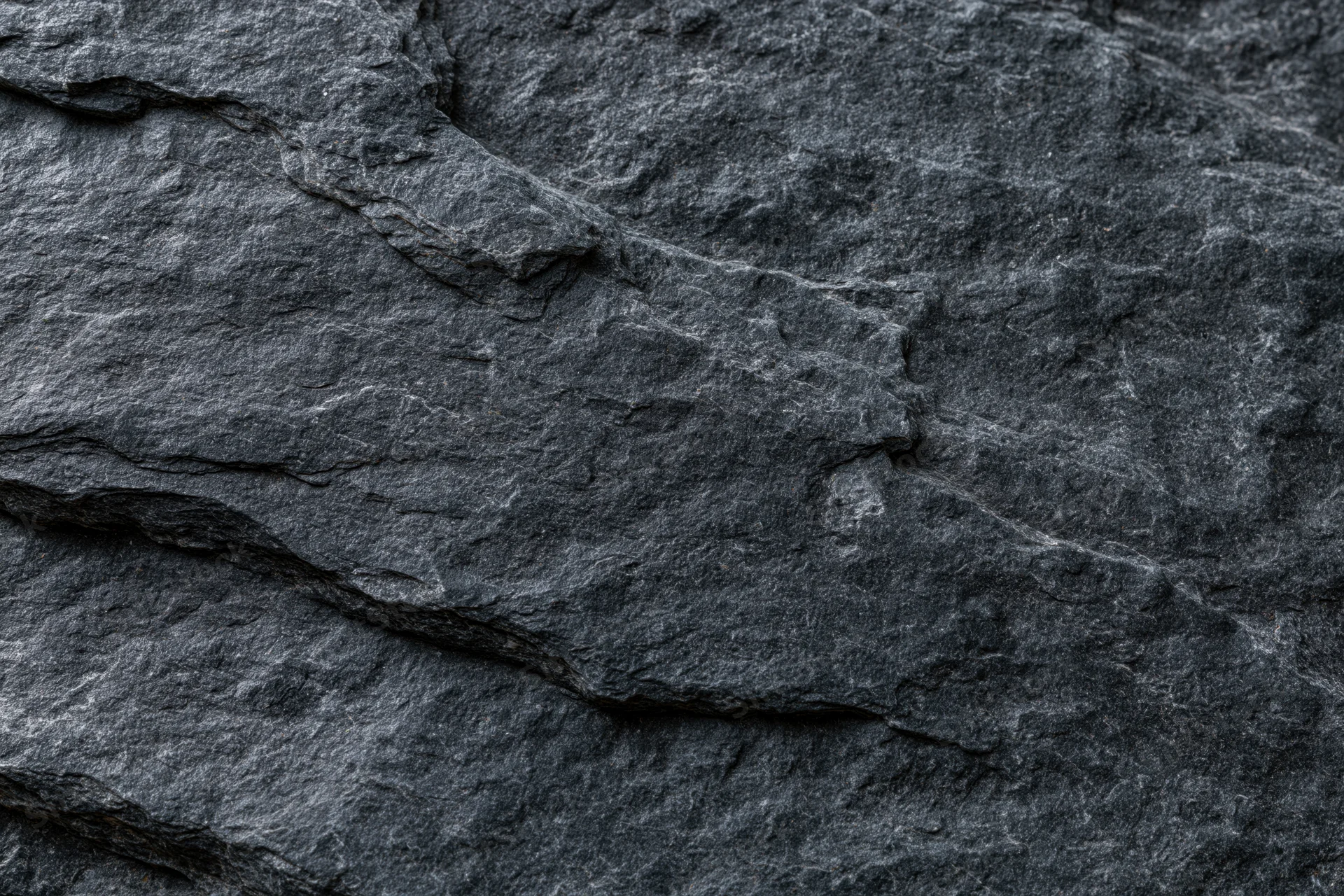 Dark slate rock surface with natural cracks and layers filling the frame