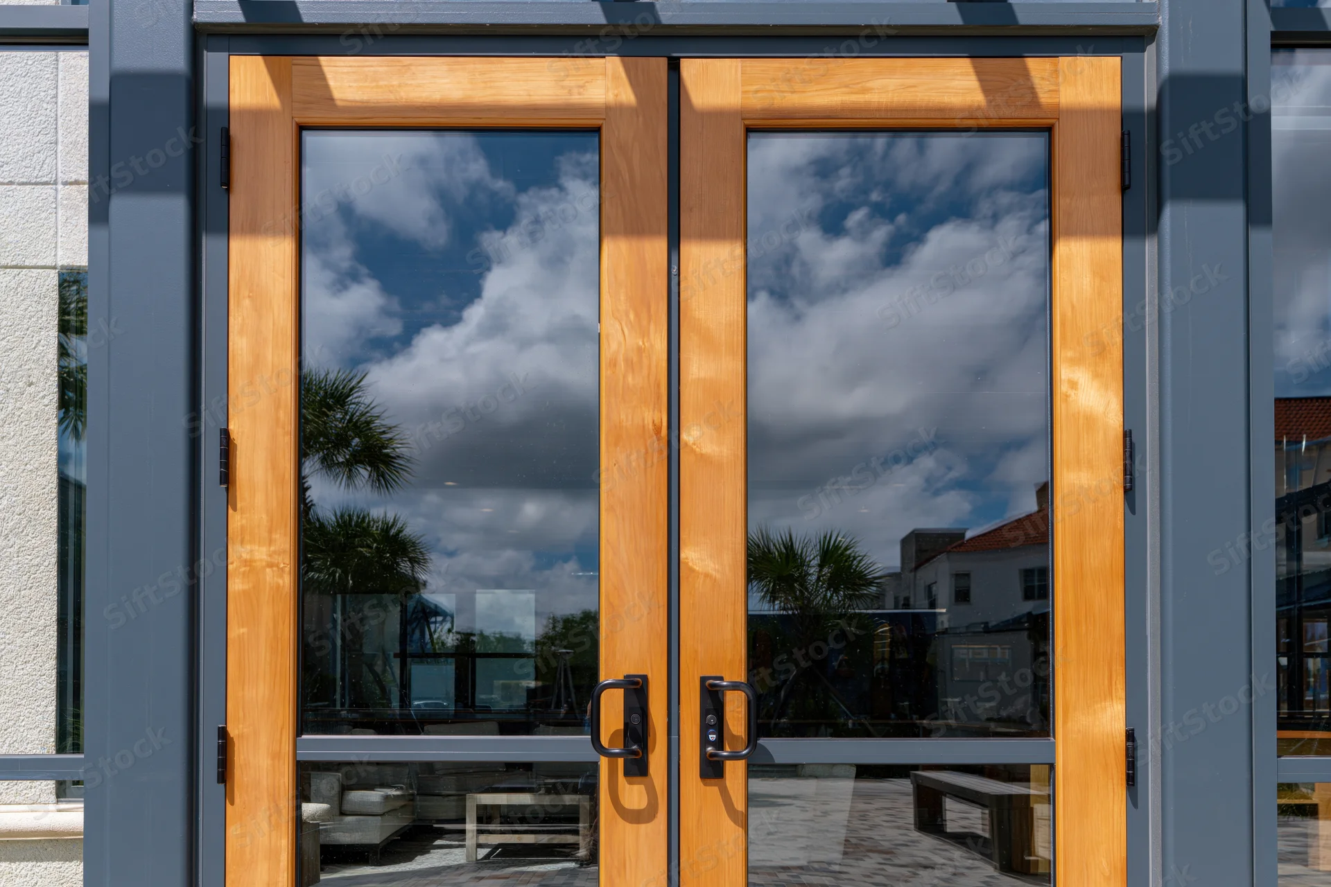 Double glass doors with wooden frames reflecting sky and clouds outside a modern building entrance