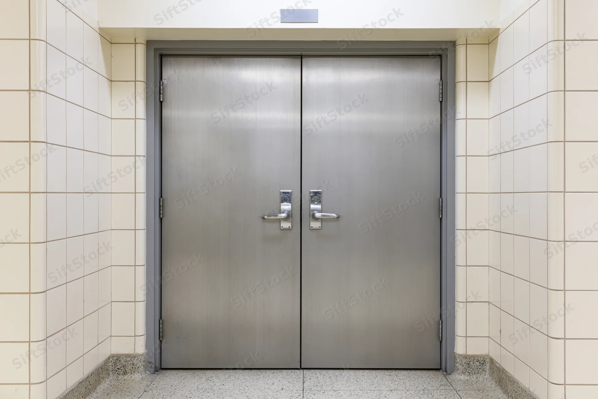 Double steel fire door with lever handles centered in a tiled hallway