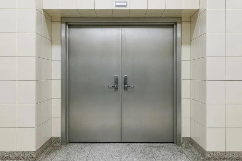 Double steel fire door with lever handles centered in a tiled institutional corridor