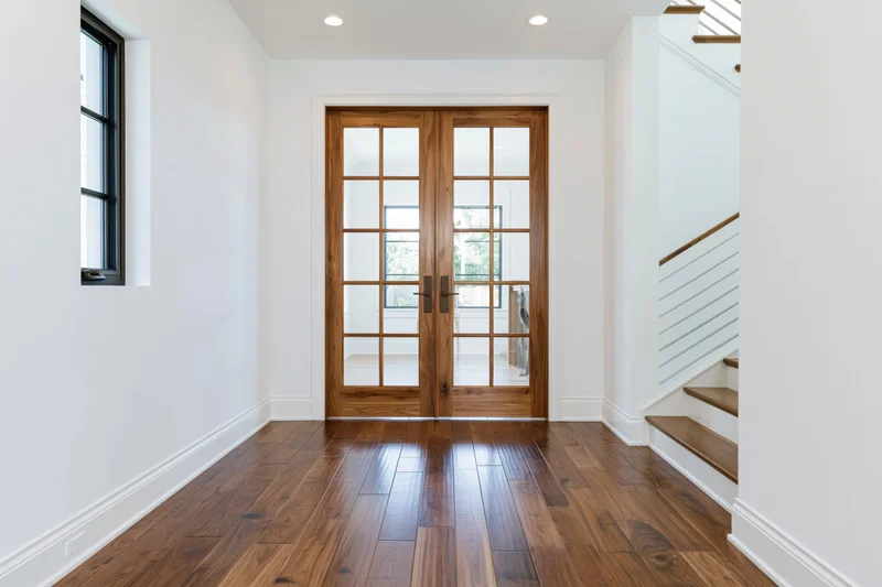 Hallway with double wood-framed french doors and hardwood floor leading to staircase