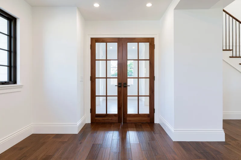 Hallway with double wood-framed french doors and hardwood flooring leading to a bright interior space