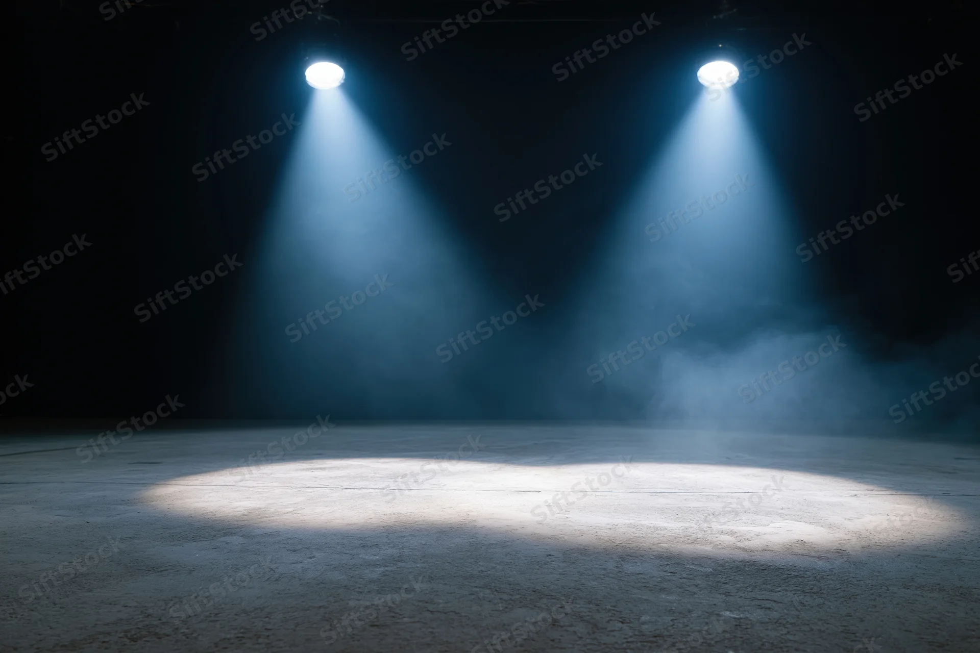 Two spotlights casting beams of light onto an empty stage floor in a dark theater