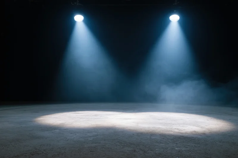 Two spotlights casting beams of light onto an empty stage floor in a dark theater