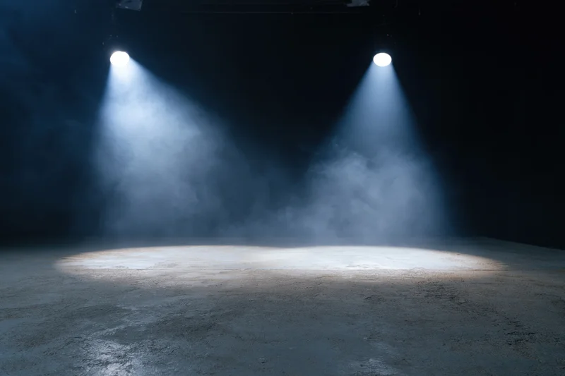 Two spotlights illuminating an empty stage floor in a dark theater