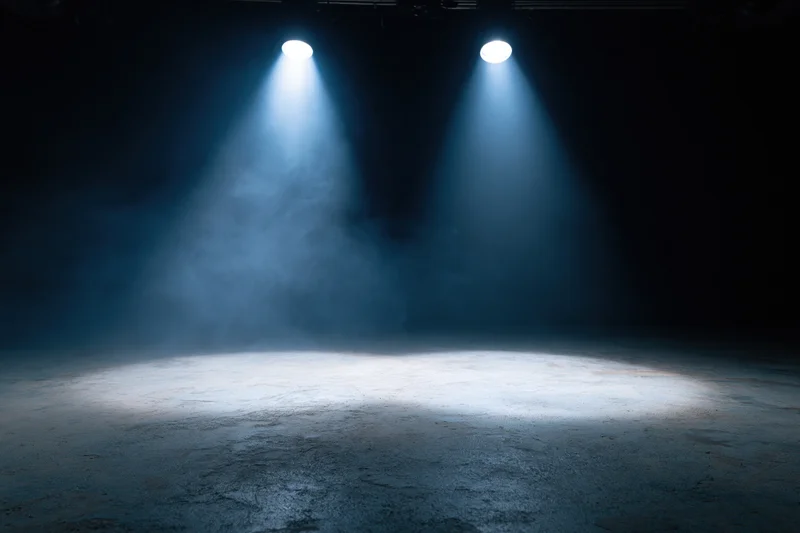 Two spotlights shining down on an empty stage floor in a dark theater