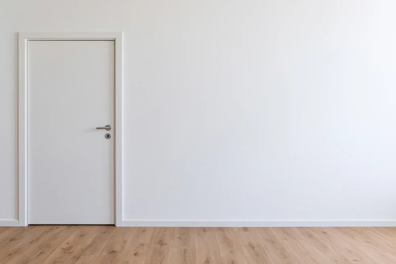 Empty interior room with a single closed white door on a wooden floor