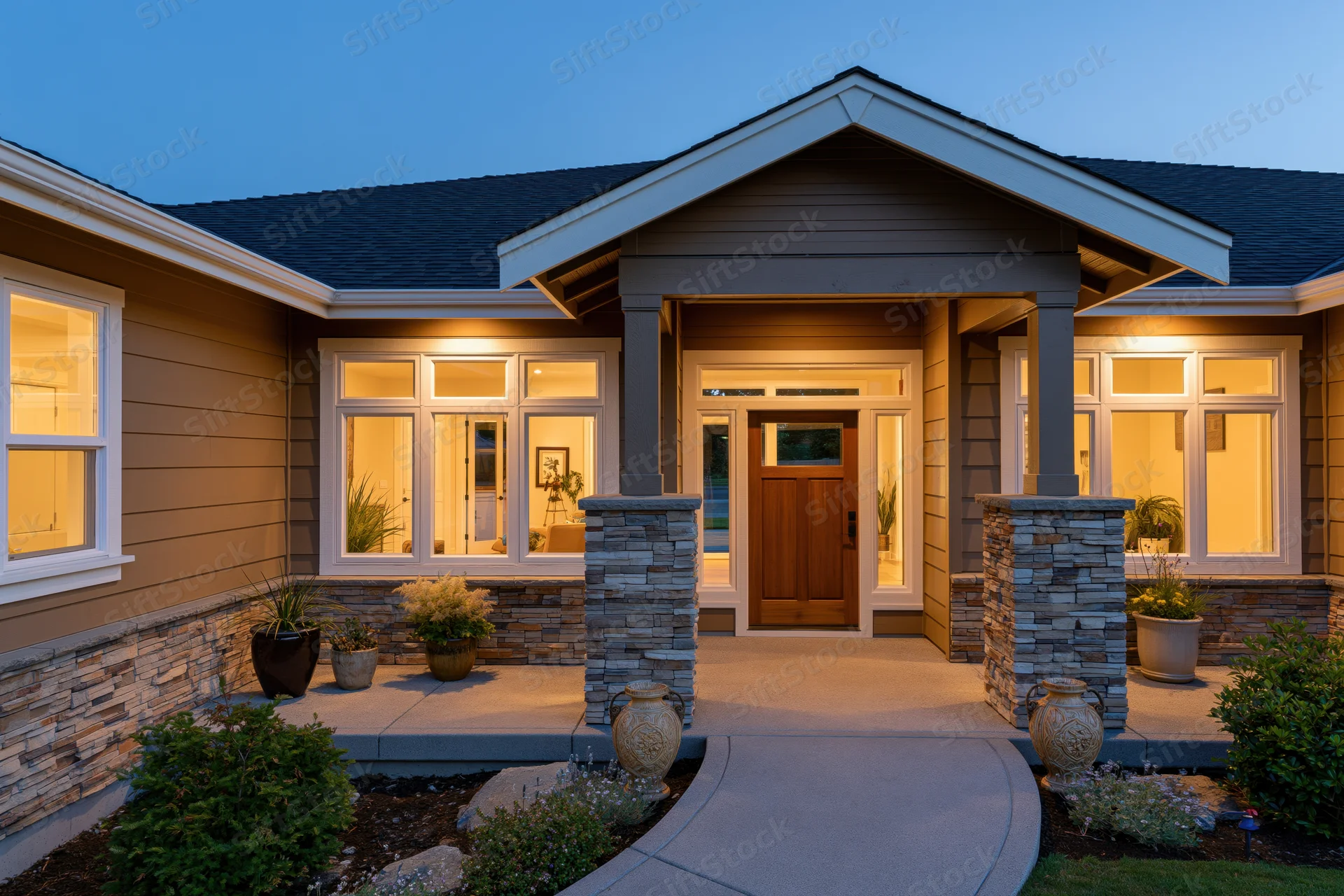 Modern craftsman home front entrance at dusk with illuminated porch and stone columns