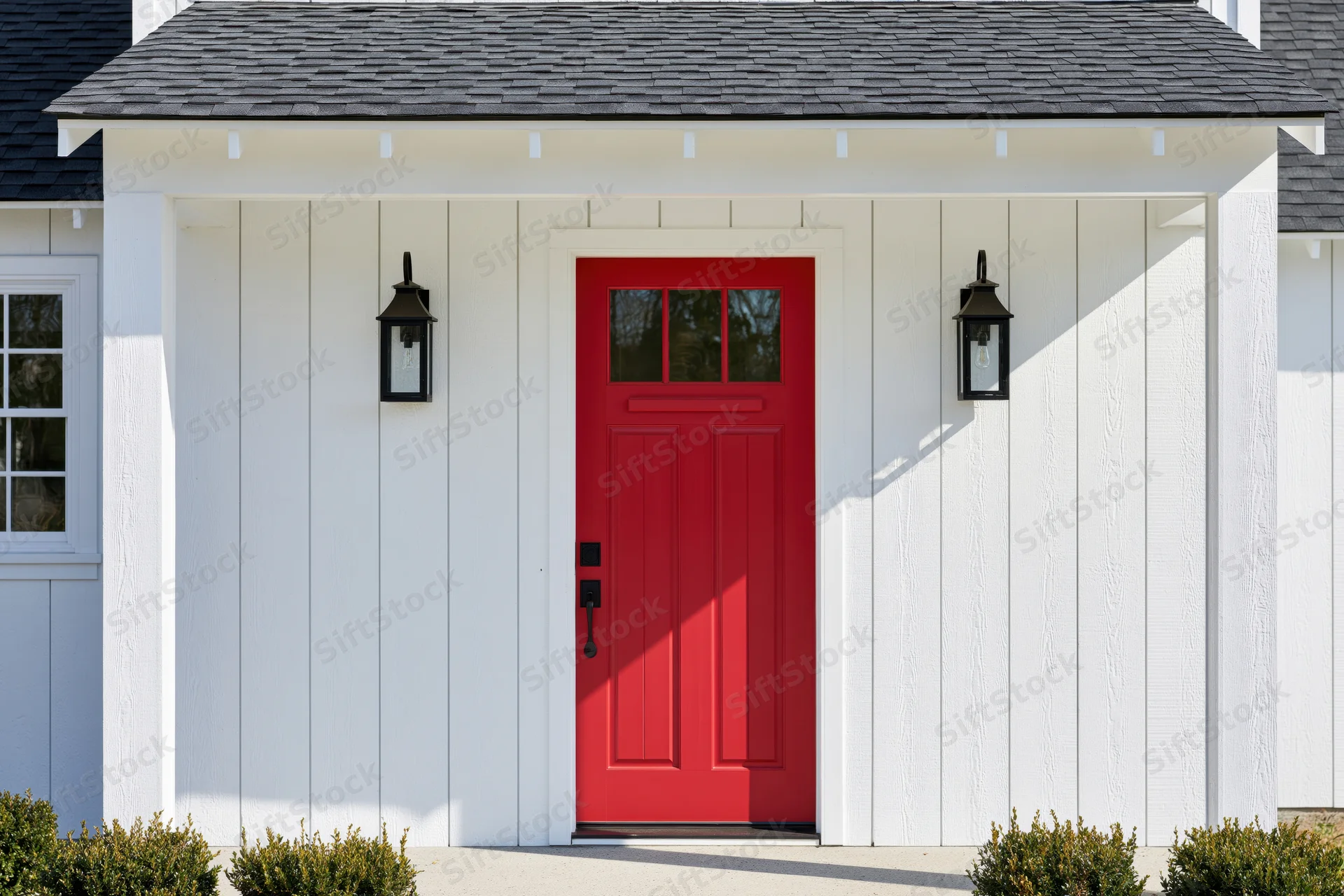 Red front door on white farmhouse-style house with black lantern lights and porch overhang
