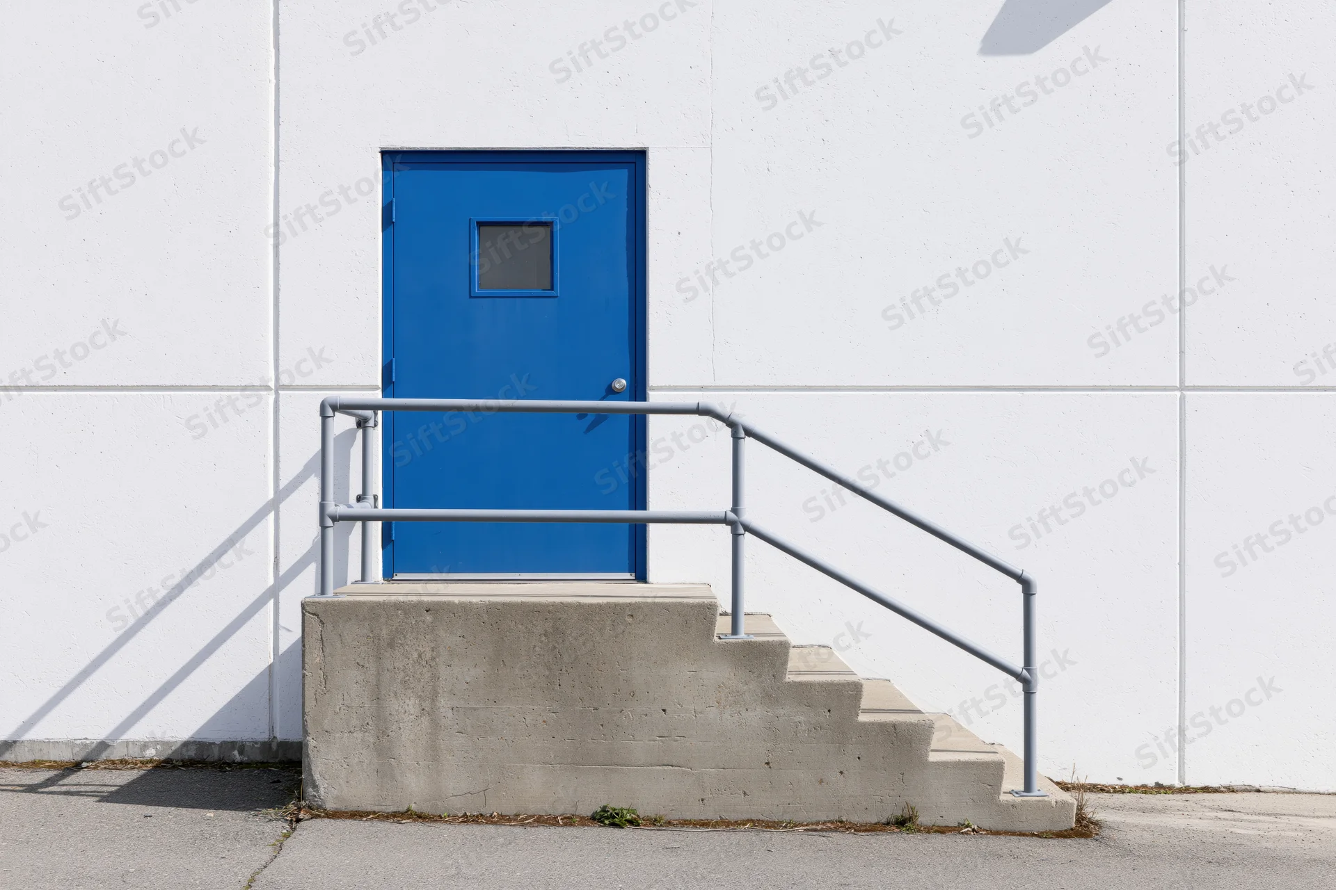 Blue door on concrete steps with metal railing at warehouse exterior