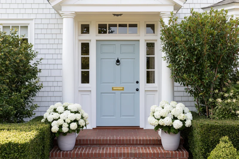 Front entrance of a classic american craftsman home with blue door and white hydrangeas on brick steps