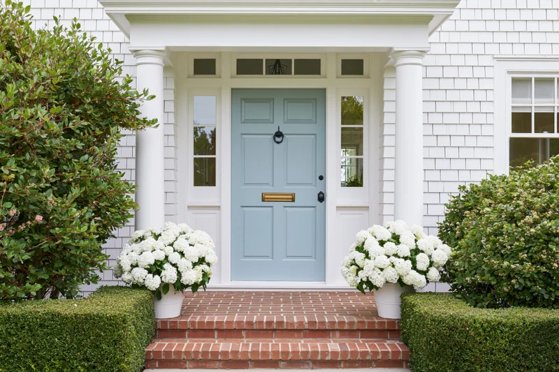 Front entrance of a classic american craftsman house with blue door and white hydrangeas on brick steps