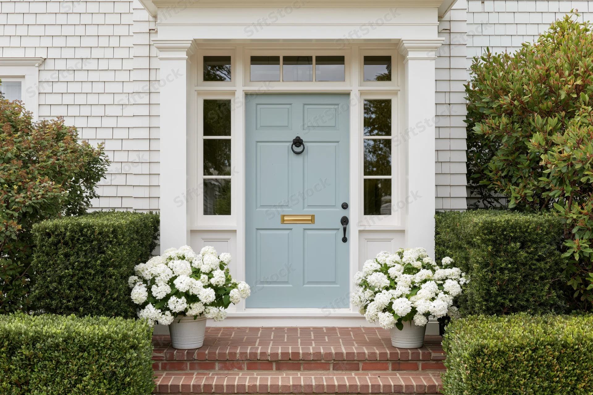 Front entrance of a classic american craftsman home with blue door and white hydrangeas on brick steps