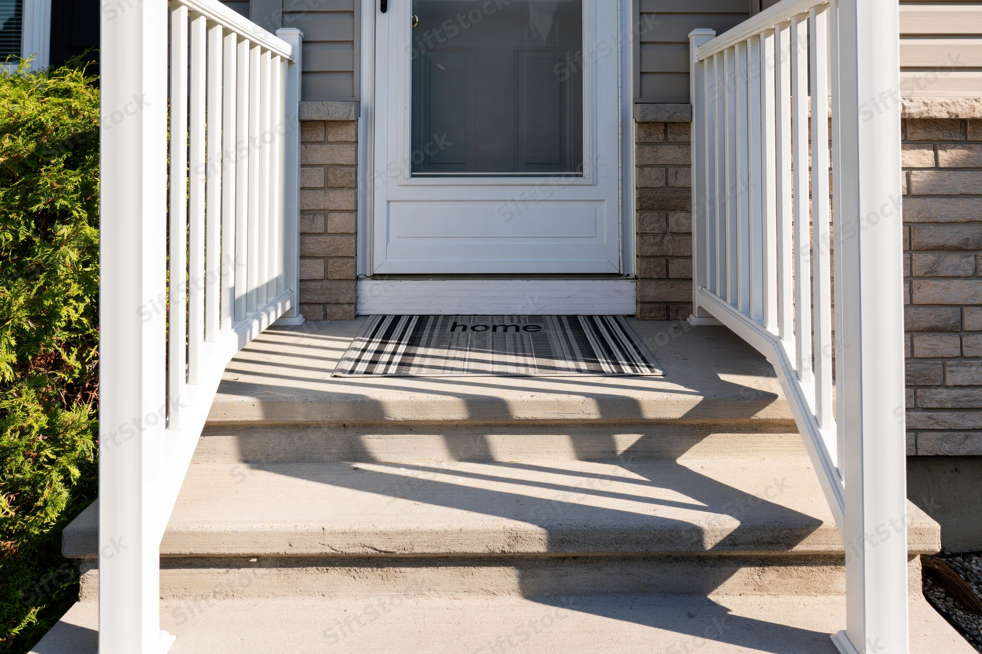 Front entrance of a suburban home with white railing and striped doormat reading home on concrete steps