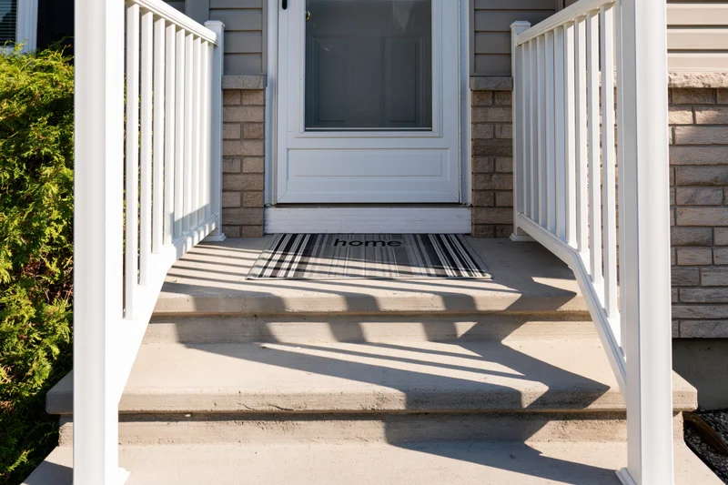 Front entrance of a suburban home with white railing and striped doormat reading home on concrete steps