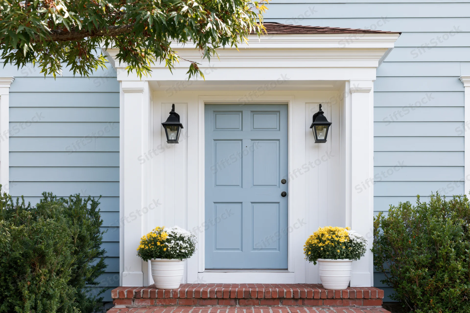 Pale blue paneled door at front entrance of suburban home with white trim, brick steps, and potted flowers on either side