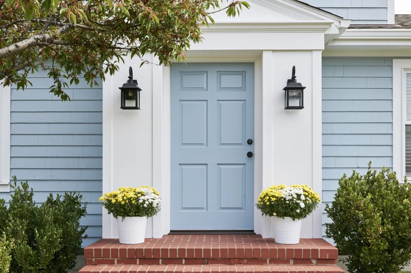 Pale blue paneled door at front entrance of suburban home with brick steps and potted flowers on either side
