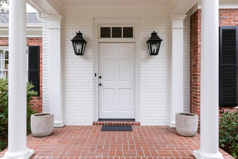White paneled front door on a brick porch with columns and lanterns at a traditional southern home
