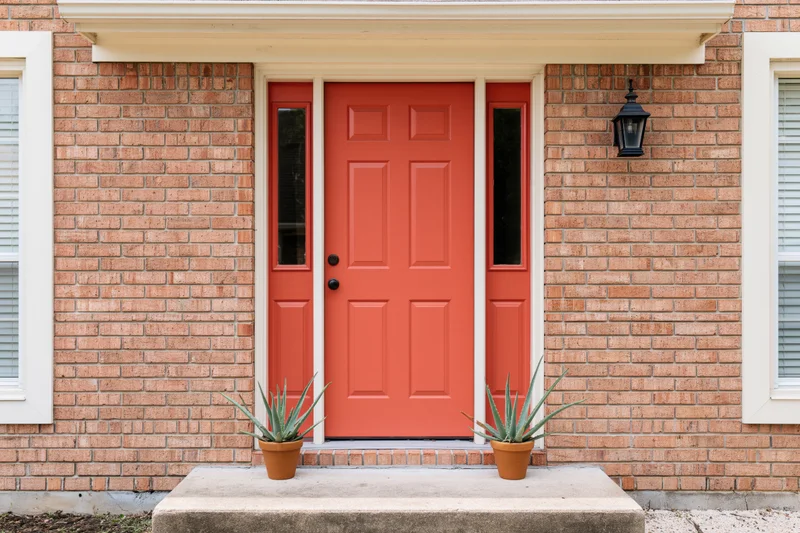 Red front door on brick suburban home with potted succulents on porch steps