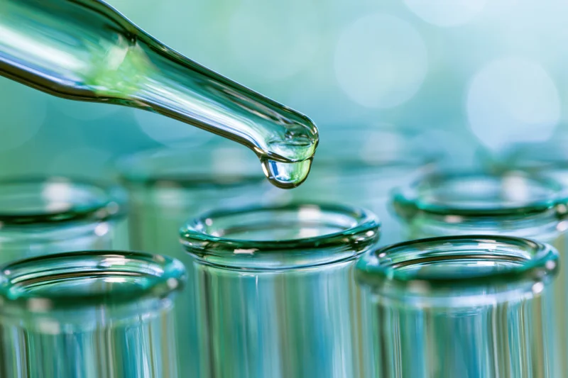 Glass dropper releasing a single drop of liquid over laboratory vials in a lab setting