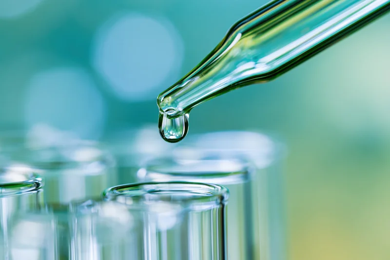Glass dropper releasing a single drop over test tubes in a laboratory setting