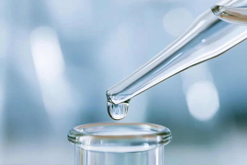 Glass pipette releasing a single droplet into a beaker in a laboratory setting