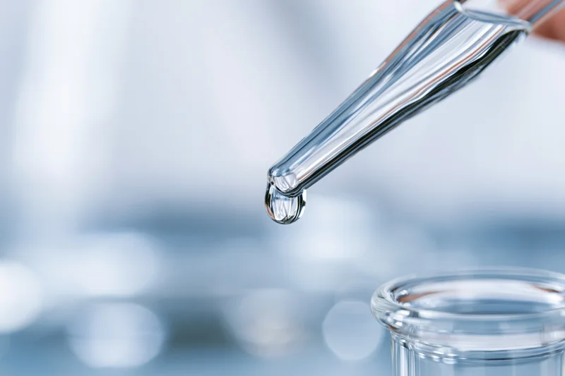 Glass pipette releasing a droplet of liquid into a beaker in a laboratory setting
