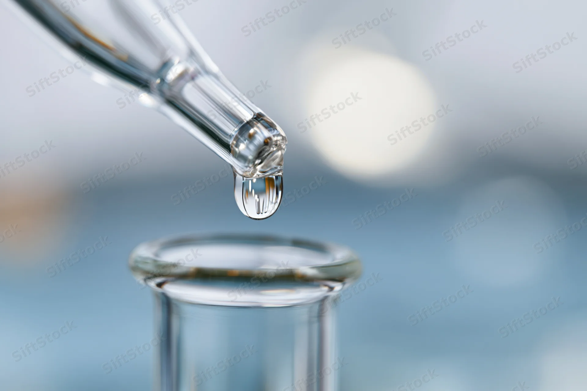 Glass pipette releasing a single droplet of liquid into a vial in a laboratory setting