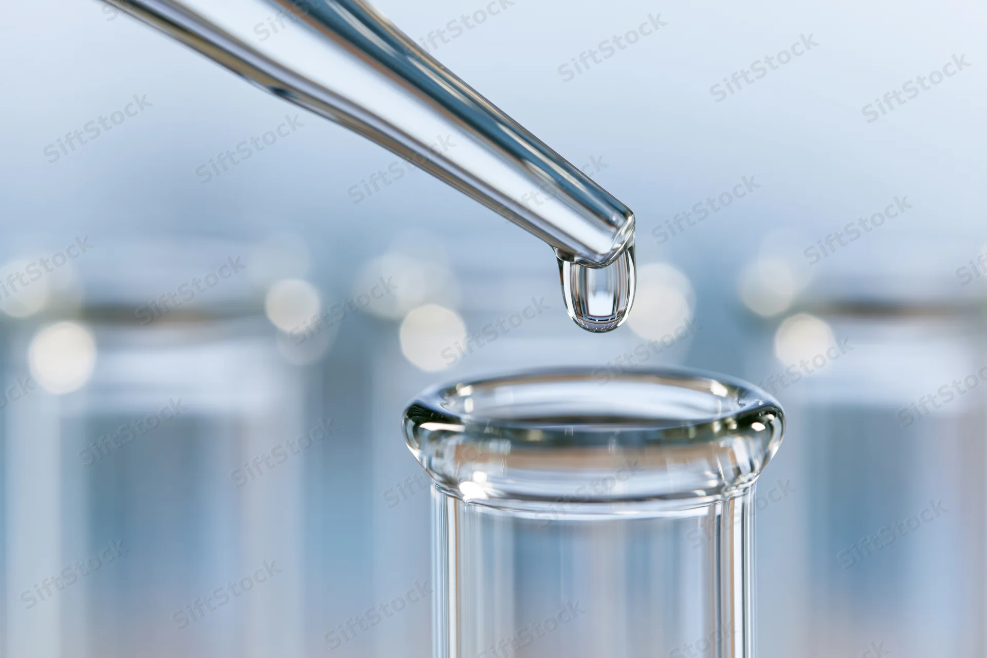 Glass pipette releasing a single droplet into a test tube in a laboratory setting