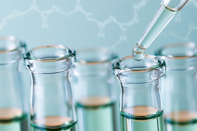 Pipette dropping liquid into a row of glass test tubes in a laboratory setting