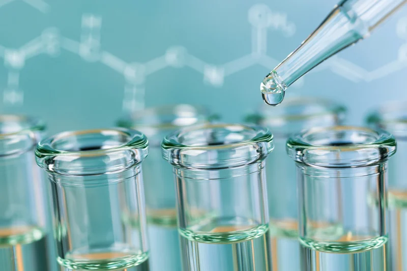 Pipette dropping liquid into a row of glass test tubes in a laboratory setting