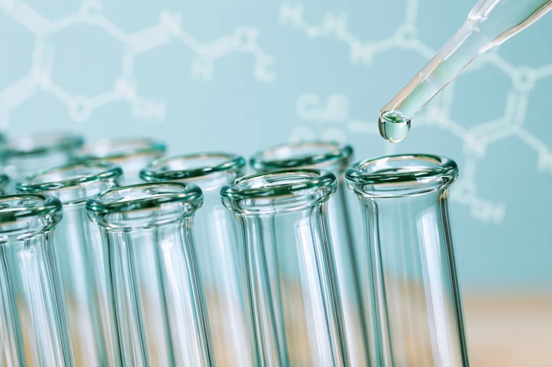 Pipette dropping liquid into a row of glass test tubes in a laboratory setting