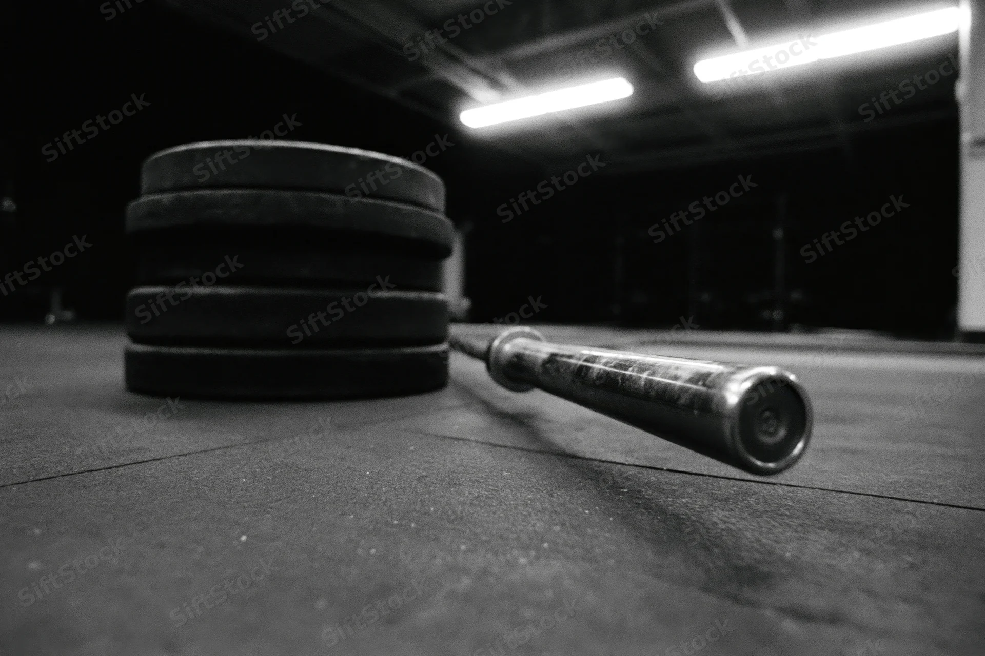 Steel barbell lying beside stacked iron weight plates on gym floor