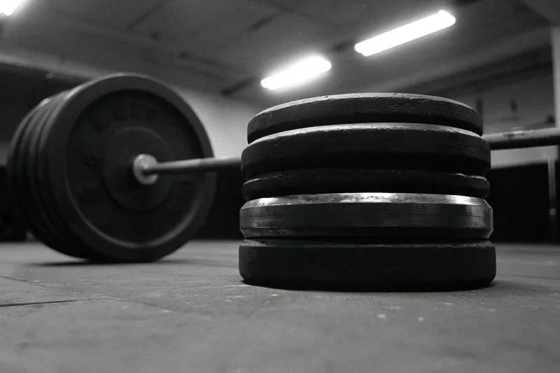 Stacked iron weight plates beside a steel barbell on a gym floor