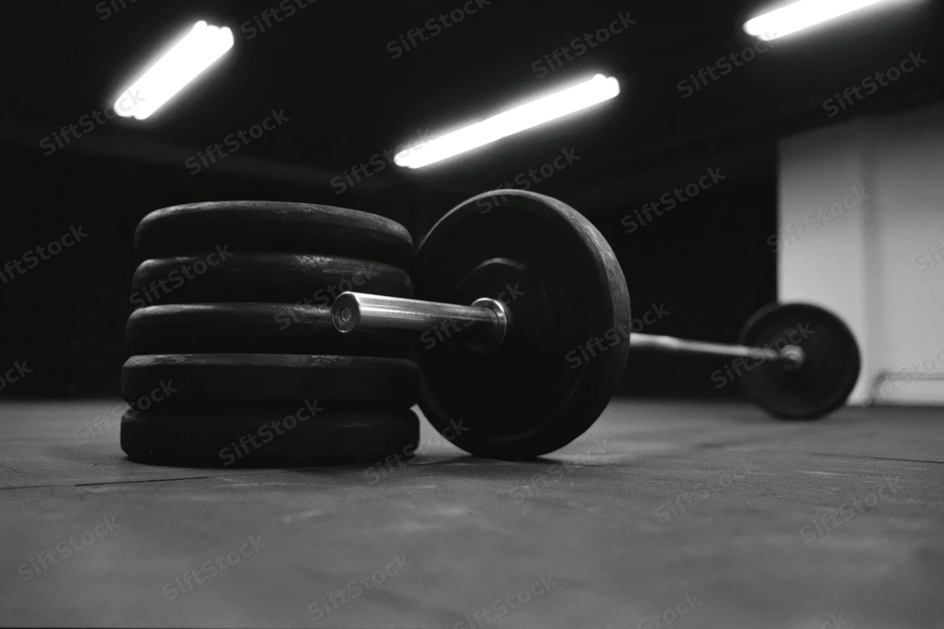 Stacked weight plates beside a steel barbell on gym floor under fluorescent lights
